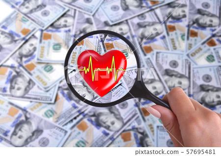 concept of Health insurance. Red heart in magnifier against the background of Many dollar banknotes 57695481