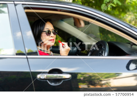 Senior woman with lipstick in her hand sitting in car during a day. Senior woman with lipstick in her hand sitting in car during a day. 57700954