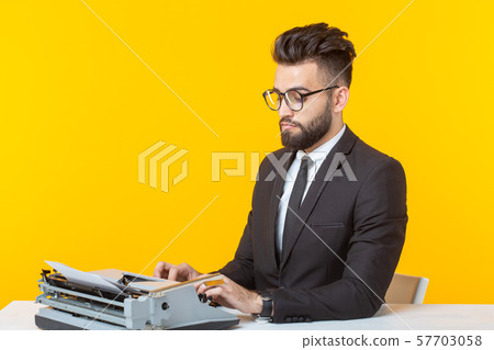Arab businessman or manager in formal suit typing text on a typewriter on a yellow background Arab businessman or manager in formal suit typing text on a typewriter on a yellow background 57703058