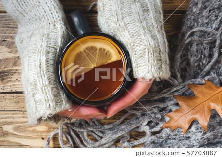 Woman's hand holding cup of tea with lemon on a cold day. Wooden table. Top view. Concept autumn 57703087