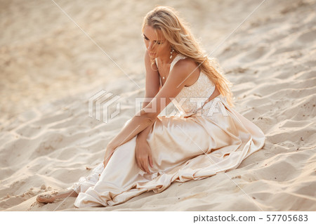 Portrait of beautiful bride is wearing fashion flying dress sitting on sand in the great desert in 57705683