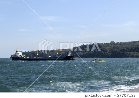 Small yellow pilot ship leads a large black cargo container ship to the seaport. 57707152
