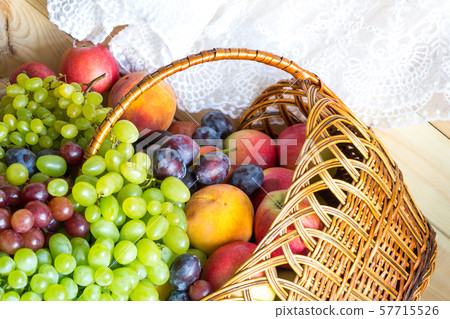 New harvest background. Heap of fresh fruits poured out from wicker basket on wooden table covered New harvest background. Heap of fresh fruits poured out from wicker basket on wooden table covered 57715526