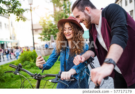 Young couple with electric scooters and smartphone in town, taking selfie. 57717179