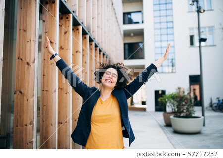 A young businesswoman standing outdoors, expressing excitement. A young businesswoman standing outdoors, expressing excitement. 57717232