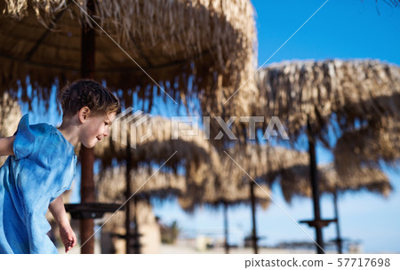 Small girl walking among straw parasols outdoors on beach. Copy space. 57717698
