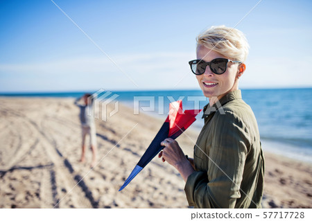 Mother with son standing outdoors on beach, playing with plane. 57717728