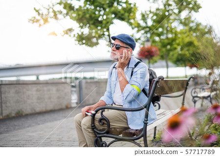 Senior blind man with smartphone sitting on bench in park in city. Senior blind man with smartphone sitting on bench in park in city. 57717789