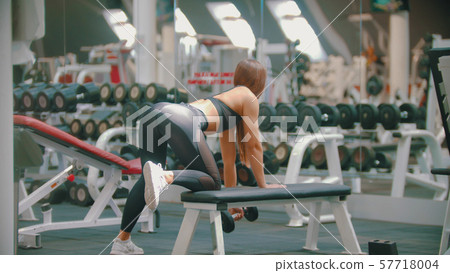 A sportive woman with long hair training in the gym - training her arms - pulling the dumbbell while A sportive woman with long hair training in the gym - training her arms - pulling the dumbbell while 57718004