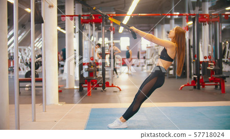 A sportive woman in sports clothes training in the gym - holding the handles and leans back 57718024