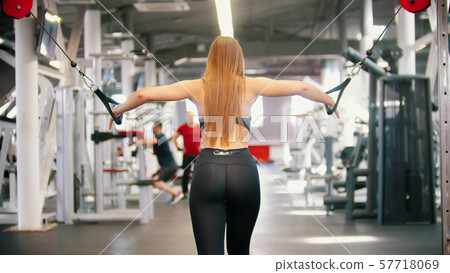 An athletic woman with long hair training in the gym - pulling the handles - training hands 57718069