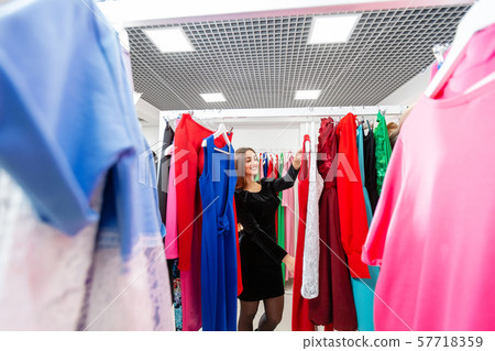 Happy young woman choosing clothes in mall or clothing store. Sale, fashion, consumerism concept Happy young woman choosing clothes in mall or clothing store. Sale, fashion, consumerism concept 57718359