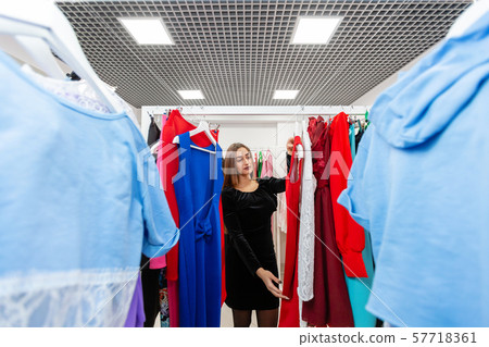 Happy young woman choosing clothes in mall or clothing store. Sale, fashion, consumerism concept 57718361
