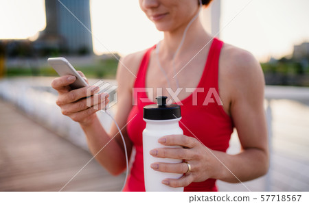 Midsection of young woman runner with earphones in city, using smartphone. Midsection of young woman runner with earphones in city, using smartphone. 57718567
