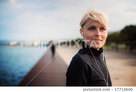 A portrait of young sportswoman with earphones standing outdoors on beach. A portrait of young sportswoman with earphones standing outdoors on beach. 57718606