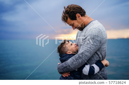 Father with small son on a walk outdoors standing on beach at dusk. 57718624