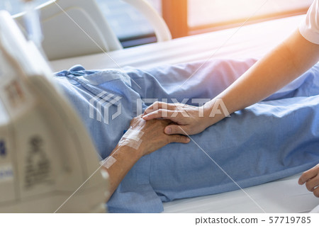 Caregiver holding elderly senior patient (ageing old adult person) hand in hospital bed or nursing hospice, geriatrician palliative home, while caretaker having medical health care service Caregiver holding elderly senior patient (ageing old adult person) hand in hospital bed or nursing hospice, geriatrician palliative home, while caretaker having medical health care service 57719785