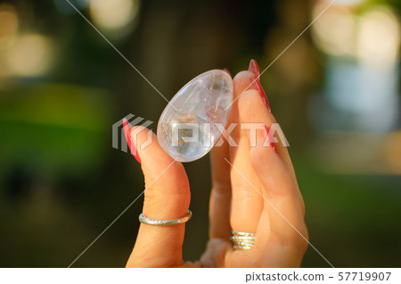 Female hand with transparent amethyst quartz yoni egg for vumfit, imbuilding or meditation. Shining 57719907
