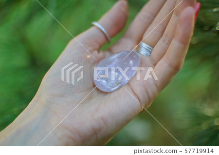 Female hand with transparent amethyst quartz yoni egg for vumfit, imbuilding or meditation. Shining 57719914