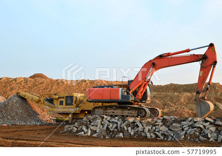 Heavy tracked excavator load stone, old asphalt or concrete waste into a mobile jaw crusher machine. Heavy tracked excavator load stone, old asphalt or concrete waste into a mobile jaw crusher machine. 57719995