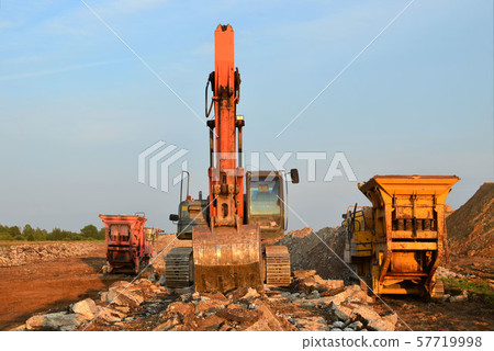 Heavy tracked excavator load stone, old asphalt or concrete waste into a mobile jaw crusher machine. Heavy tracked excavator load stone, old asphalt or concrete waste into a mobile jaw crusher machine. 57719998