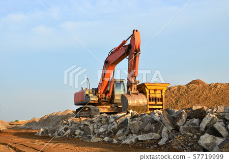 Heavy tracked excavator load stone, old asphalt or concrete waste into a mobile jaw crusher machine. Heavy tracked excavator load stone, old asphalt or concrete waste into a mobile jaw crusher machine. 57719999