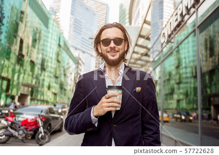 Photo of happy brunet with beard and earring in ear from glass in hand in city against background of 57722628