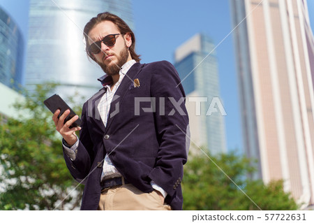 Photo of man in sunglasses with phone in his hand looking into camera for walk in city 57722631