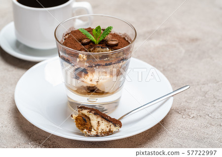 Portion of Classic tiramisu dessert in a glass and cup of coffee on concrete background Portion of Classic tiramisu dessert in a glass and cup of coffee on concrete background 57722997