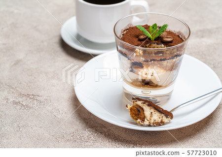 Portion of Classic tiramisu dessert in a glass and cup of coffee on concrete background 57723010