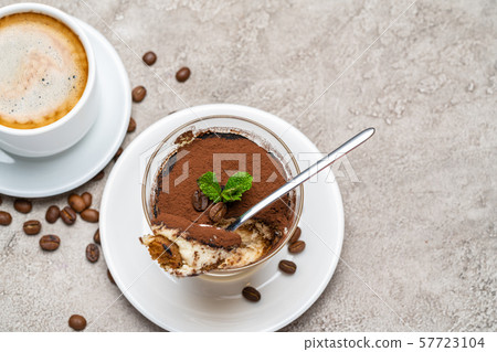 Portion of Classic tiramisu dessert in a glass and cup of coffee on concrete background Portion of Classic tiramisu dessert in a glass and cup of coffee on concrete background 57723104