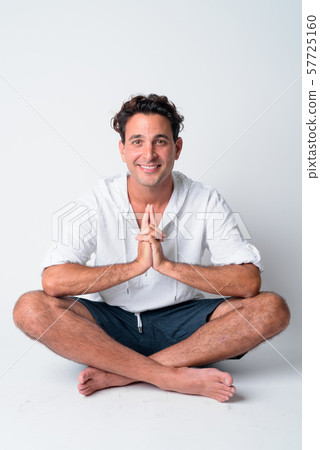 Full body shot of happy handsome Hispanic man smiling while sitting with legs crossed Full body shot of happy handsome Hispanic man smiling while sitting with legs crossed 57725160