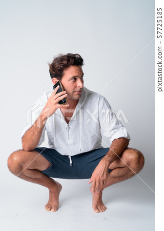 Full body shot of handsome Hispanic man crouching while talking on the phone Full body shot of handsome Hispanic man crouching while talking on the phone 57725185