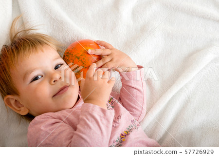 Cute little girl hugging a pumpkin on a bed indoors. copy space Cute little girl hugging a pumpkin on a bed indoors. copy space 57726929