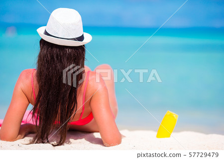 Beautiful young woman holding a suncream lying on tropical beach Beautiful young woman holding a suncream lying on tropical beach 57729479