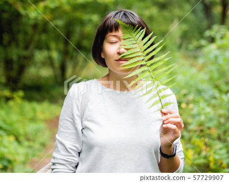 Young woman is hiding her eye with fern leaf. Young woman is hiding her eye with fern leaf. 57729907