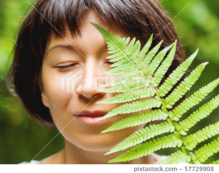 Young woman is hiding her eye with fern leaf. 57729908