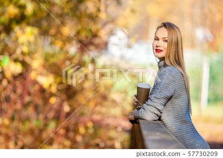 Fall concept - beautiful woman drinking coffee in autumn park under fall foliage Fall concept - beautiful woman drinking coffee in autumn park under fall foliage 57730209