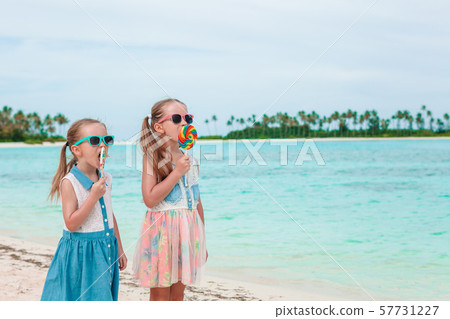 Two little girls eating bright lollipops on the beach Two little girls eating bright lollipops on the beach 57731227