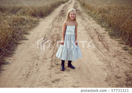 blonde girl stands on an earthen path in a long dress among a wheat field blonde girl stands on an earthen path in a long dress among a wheat field 57731321