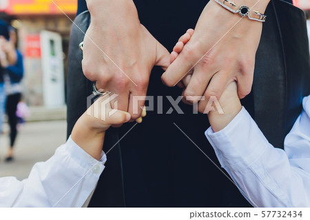 Hands of mother and daughter holding each other. Summer park in background. 57732434