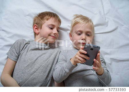 Two boys are lying in bed with a smartphone. Two boys are lying in bed with a smartphone. 57733393