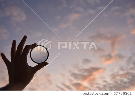 silhouette of female hand holding the lens and the sky on the background at the time of the sunset silhouette of female hand holding the lens and the sky on the background at the time of the sunset 57739561