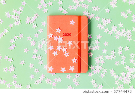 Orange diary for 2020 on a mint background strewn with light pink stars. 57744473