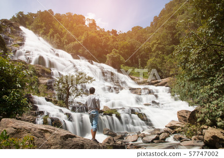 Young standing on stone and looking at waterfall Young standing on stone and looking at waterfall 57747002