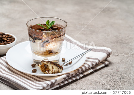 Portion of Classic tiramisu dessert in a glass cup on concrete background Portion of Classic tiramisu dessert in a glass cup on concrete background 57747006