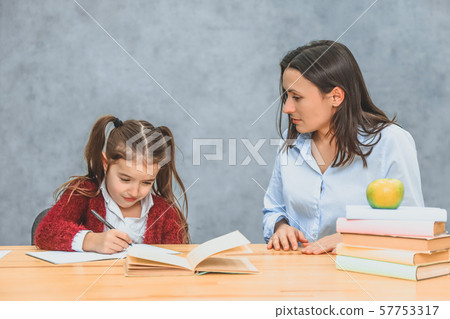 Young mother and daughter sitting on a gray background. During this, the mother watches over how a Young mother and daughter sitting on a gray background. During this, the mother watches over how a 57753317