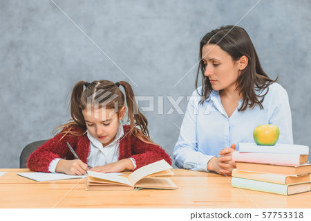 Young mother and daughter sitting on a gray background. During this, the mother watches over how a Young mother and daughter sitting on a gray background. During this, the mother watches over how a 57753318