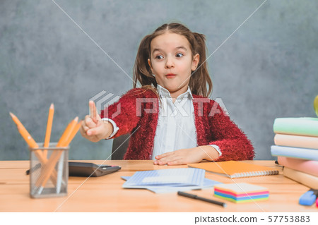 Schoolgirl girl sits at a gray background. During this, the index finger shows a yellow pencil 57753883
