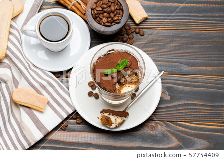 Portion of Classic tiramisu dessert in a glass, cup of coffee and savoiardi cookies on wooden Portion of Classic tiramisu dessert in a glass, cup of coffee and savoiardi cookies on wooden 57754409